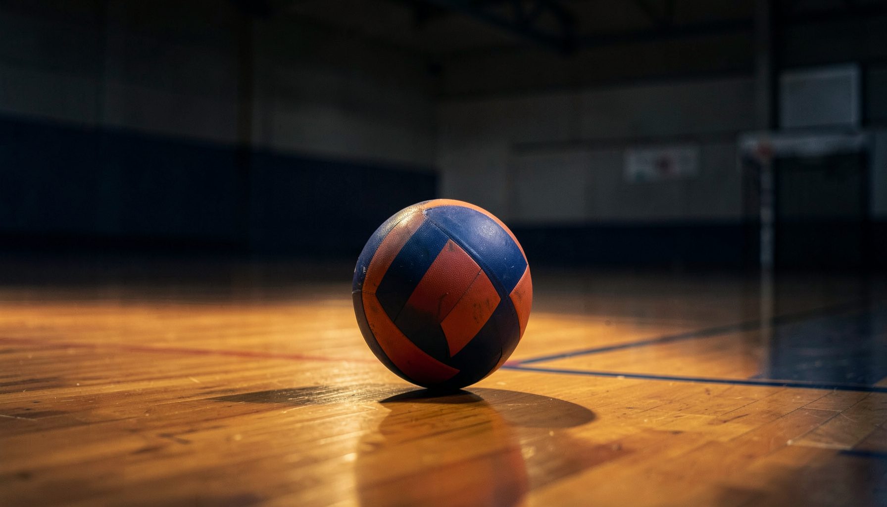 A softly lit gymnasium with a volleyball resting on the polished wooden court, warm amber tones blending with deep navy shadows