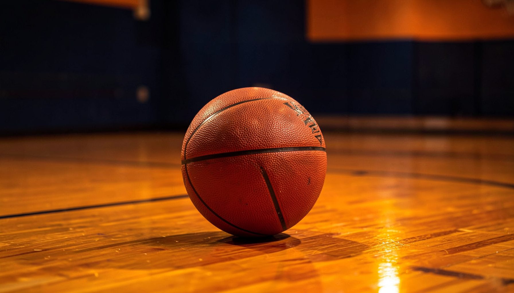 A smart basketball resting on a polished indoor court, warm amber court lights reflecting off the surface, deep navy and orange tones in the background
